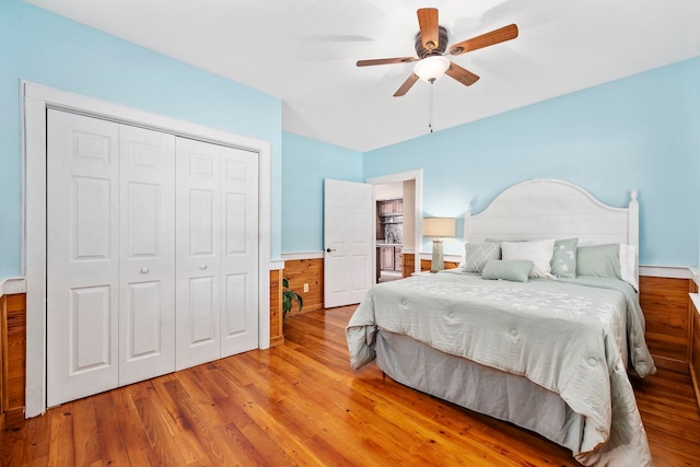 bedroom with a closet, ceiling fan, wooden walls, and light hardwood / wood-style floors