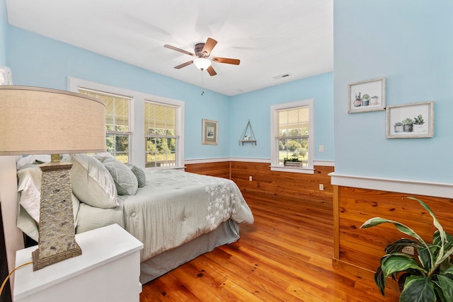 bedroom with ceiling fan, wood walls, and hardwood / wood-style flooring