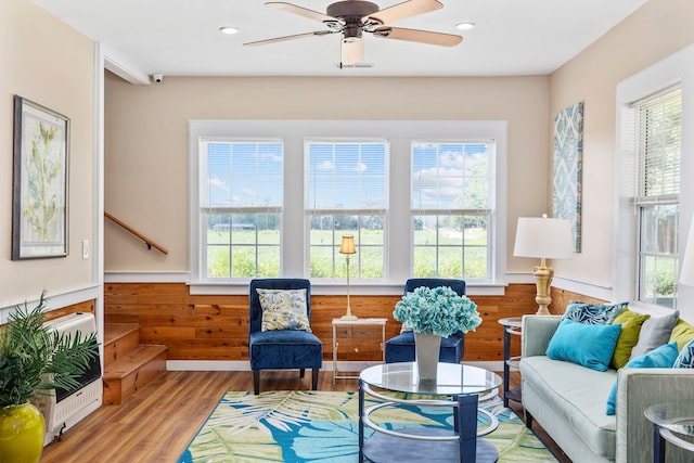 living area featuring wood-type flooring, heating unit, ceiling fan, and wooden walls