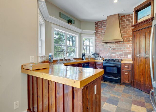 kitchen featuring custom exhaust hood, sink, kitchen peninsula, black range oven, and stainless steel fridge with ice dispenser