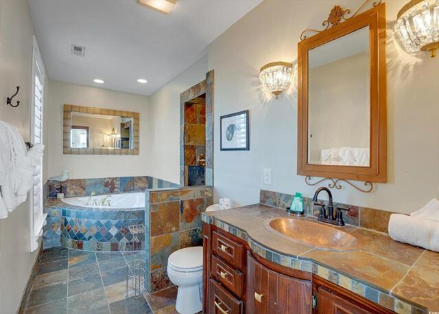 bathroom featuring toilet, tiled bath, and vanity