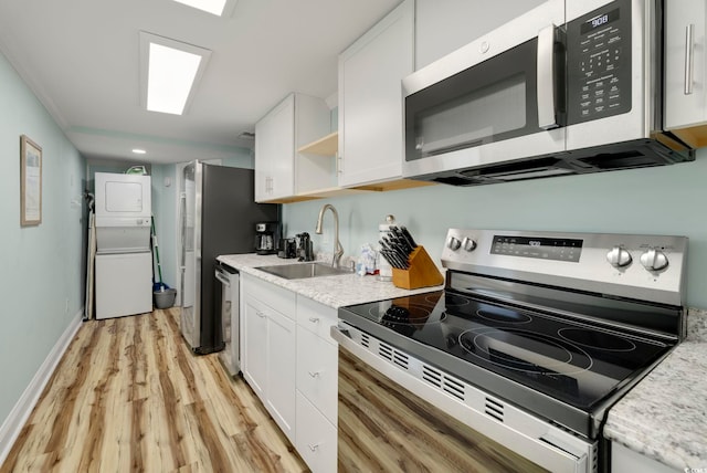 kitchen featuring sink, light hardwood / wood-style flooring, white cabinetry, stacked washing maching and dryer, and stainless steel appliances