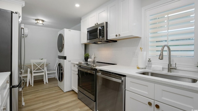 kitchen with stainless steel appliances, stacked washer and dryer, white cabinetry, and a healthy amount of sunlight