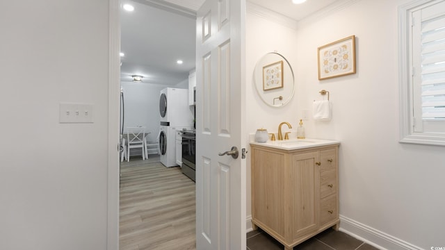 bathroom featuring ornamental molding, vanity, hardwood / wood-style floors, and stacked washing maching and dryer