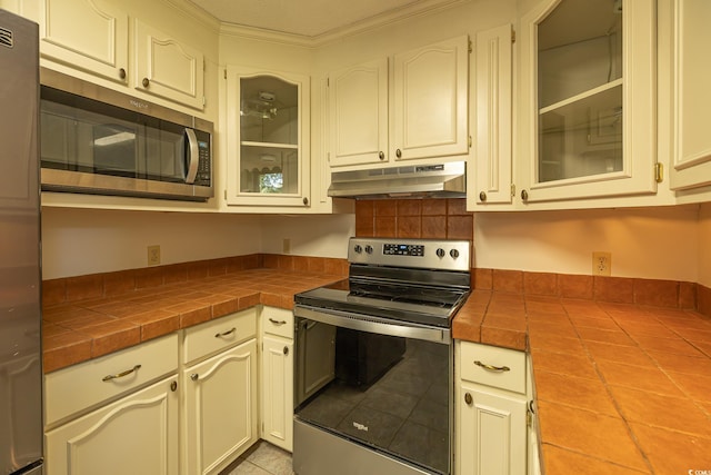 kitchen with crown molding, tile counters, light tile patterned flooring, and appliances with stainless steel finishes