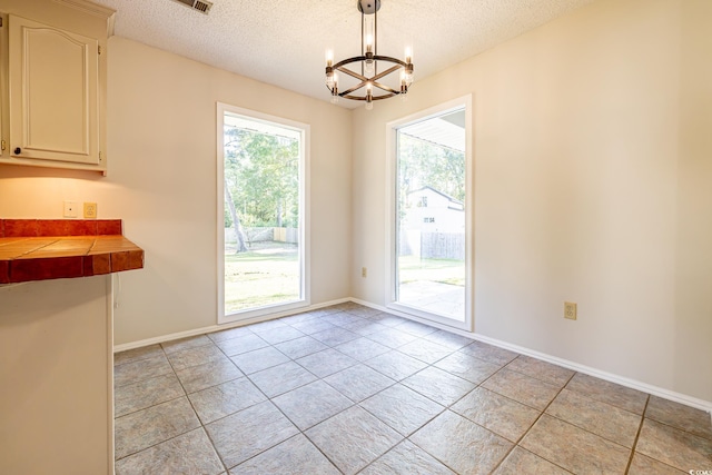 doorway to outside with a notable chandelier, light tile patterned floors, and a textured ceiling