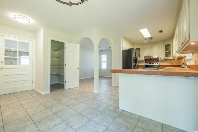 kitchen featuring light tile patterned flooring, kitchen peninsula, stainless steel electric range oven, and fridge with ice dispenser