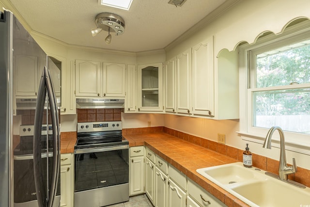 kitchen with appliances with stainless steel finishes, crown molding, sink, light tile patterned floors, and tile countertops