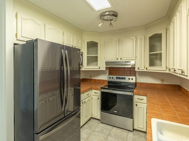 kitchen featuring tile counters, crown molding, light tile patterned floors, and stainless steel appliances