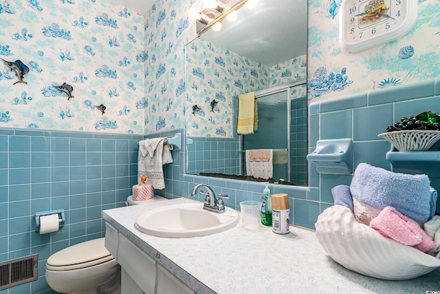 bathroom with toilet, vanity, an enclosed shower, and tile walls