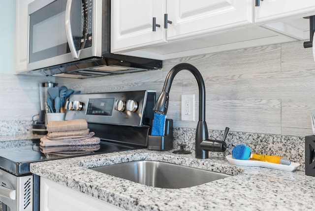 interior details with backsplash, light stone counters, sink, and white cabinets