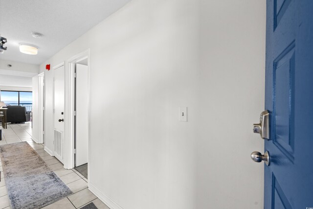 hallway with a textured ceiling and light tile patterned flooring