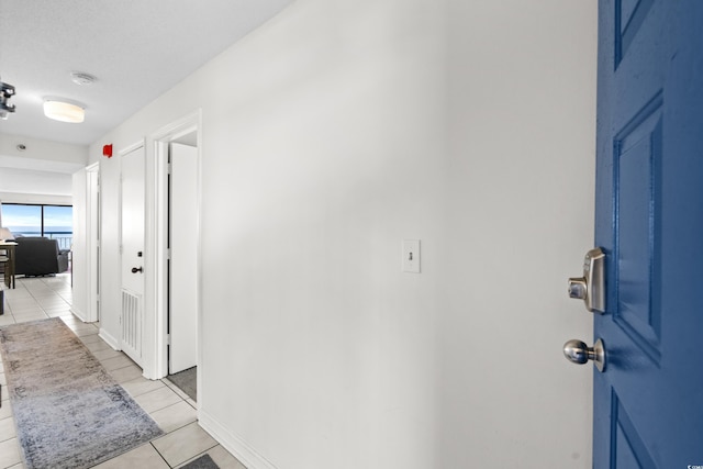 corridor with a textured ceiling, light tile patterned flooring, and baseboards