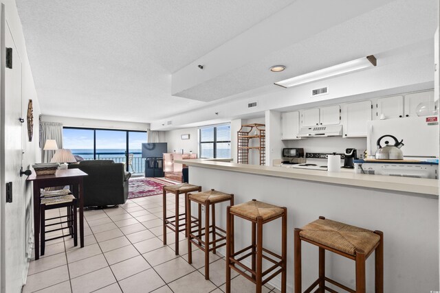 kitchen featuring white appliances, a kitchen bar, kitchen peninsula, white cabinetry, and light tile patterned flooring