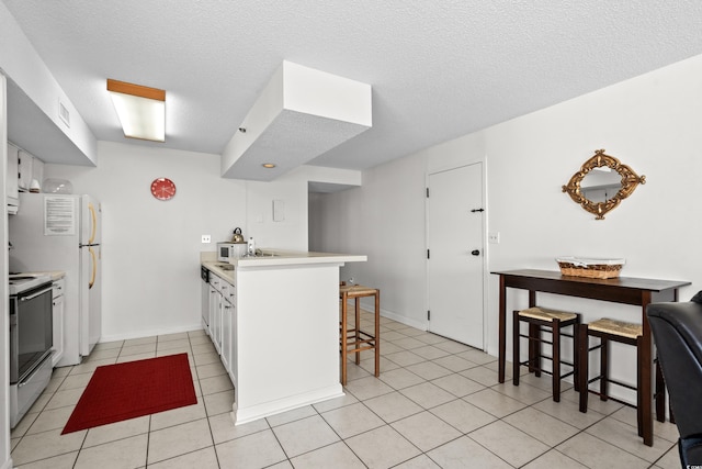 kitchen featuring a textured ceiling, a breakfast bar, kitchen peninsula, stainless steel range oven, and white cabinets