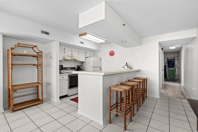 kitchen featuring kitchen peninsula, white appliances, a kitchen bar, and white cabinetry