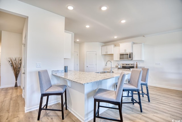 kitchen with kitchen peninsula, appliances with stainless steel finishes, a breakfast bar area, white cabinets, and light wood-type flooring