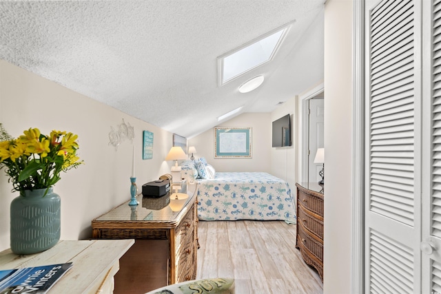 bedroom featuring light wood-type flooring, vaulted ceiling with skylight, and a textured ceiling