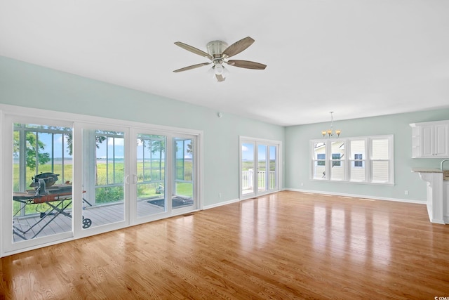 unfurnished living room with ceiling fan with notable chandelier, a wealth of natural light, and light hardwood / wood-style floors