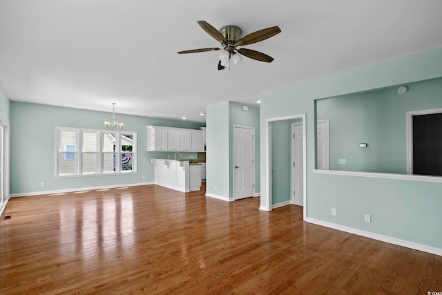 unfurnished living room featuring ceiling fan with notable chandelier, sink, and hardwood / wood-style flooring