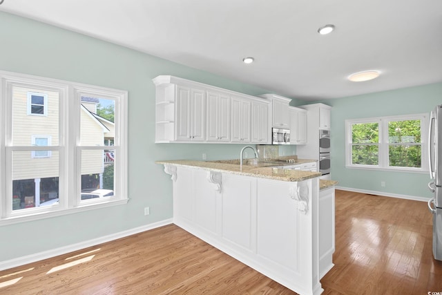 kitchen featuring white cabinets, kitchen peninsula, a breakfast bar area, stainless steel appliances, and light hardwood / wood-style flooring