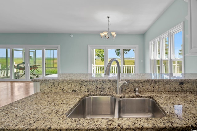 kitchen featuring light stone counters, sink, hanging light fixtures, an inviting chandelier, and hardwood / wood-style floors