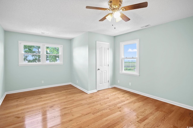 spare room with a textured ceiling, light hardwood / wood-style flooring, ceiling fan, and plenty of natural light