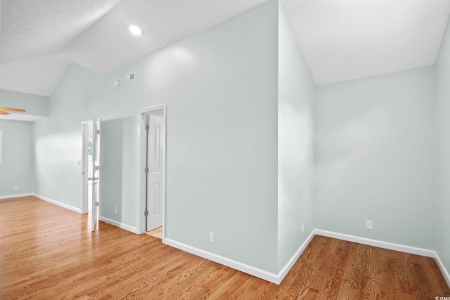 empty room with high vaulted ceiling, light hardwood / wood-style floors, and a textured ceiling