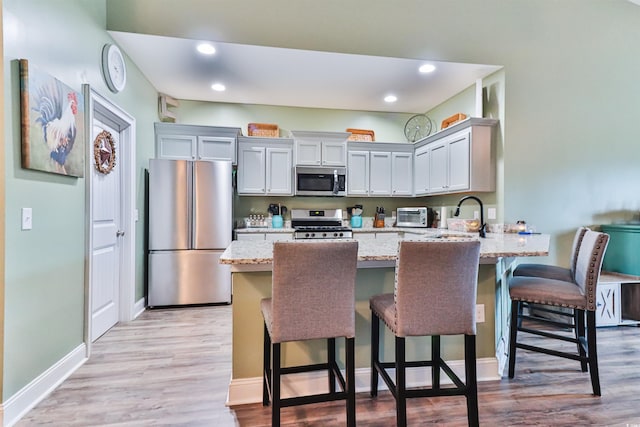 kitchen featuring light wood-type flooring, sink, stainless steel appliances, light stone countertops, and a kitchen bar