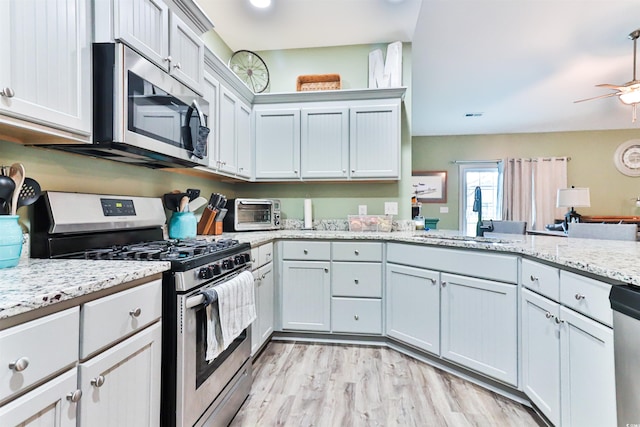 kitchen with light stone counters, sink, light hardwood / wood-style flooring, appliances with stainless steel finishes, and ceiling fan