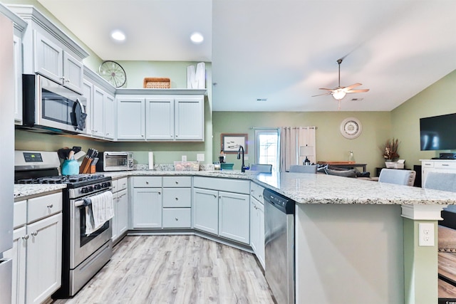 kitchen with a kitchen breakfast bar, kitchen peninsula, stainless steel appliances, light wood-type flooring, and ceiling fan