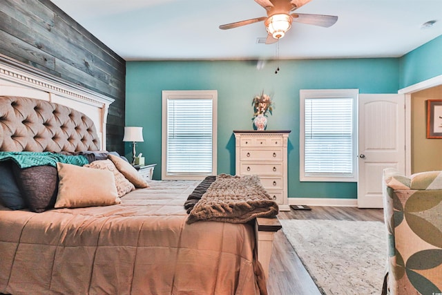 bedroom with light wood-type flooring, wooden walls, and ceiling fan