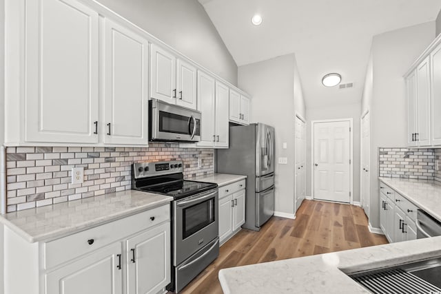 kitchen with appliances with stainless steel finishes, tasteful backsplash, white cabinets, and lofted ceiling