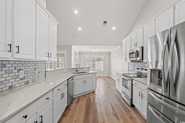 kitchen with appliances with stainless steel finishes, sink, decorative backsplash, lofted ceiling, and white cabinets