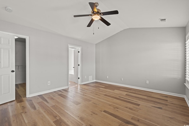 unfurnished bedroom featuring a walk in closet, light hardwood / wood-style floors, ensuite bath, lofted ceiling, and ceiling fan