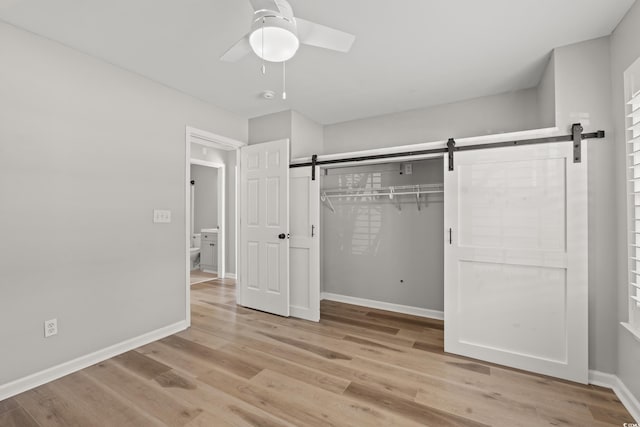 unfurnished bedroom with a barn door, ceiling fan, a closet, and light hardwood / wood-style floors