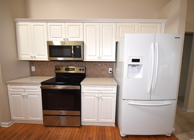 kitchen featuring light wood-style flooring, stainless steel appliances, white cabinets, light countertops, and backsplash