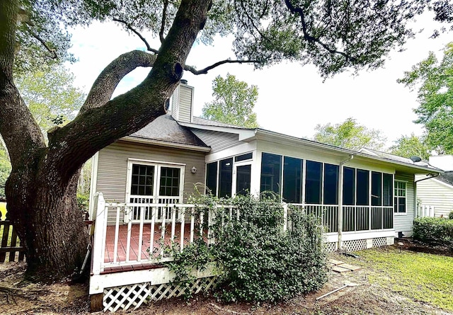 view of property exterior with a sunroom, a chimney, and a deck