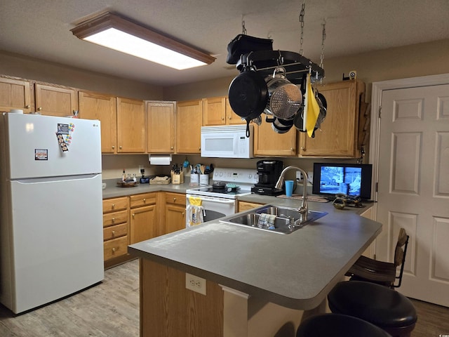 kitchen with sink, white appliances, a breakfast bar area, light brown cabinetry, and light wood-type flooring
