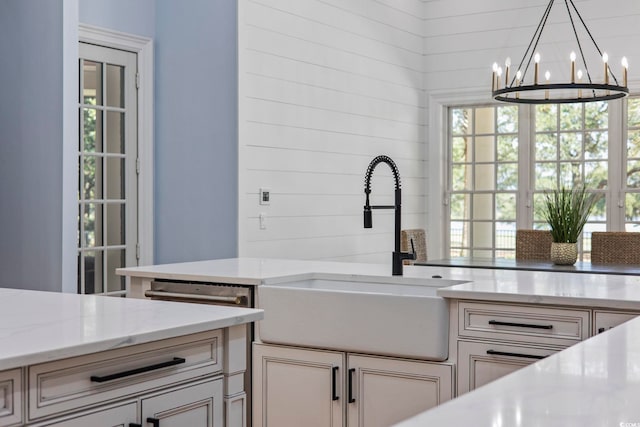 kitchen featuring wooden walls, decorative light fixtures, light stone counters, an inviting chandelier, and sink