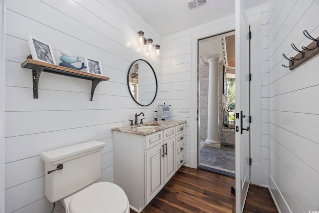 bathroom featuring toilet, wood-type flooring, decorative columns, wood walls, and vanity