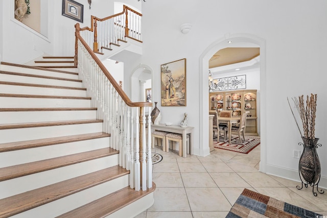 stairway with tile patterned flooring, a towering ceiling, and a tray ceiling