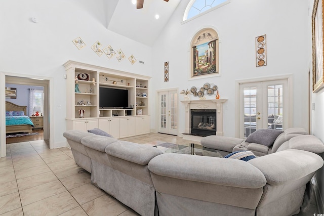 tiled living room featuring a fireplace, french doors, built in shelves, ceiling fan, and high vaulted ceiling