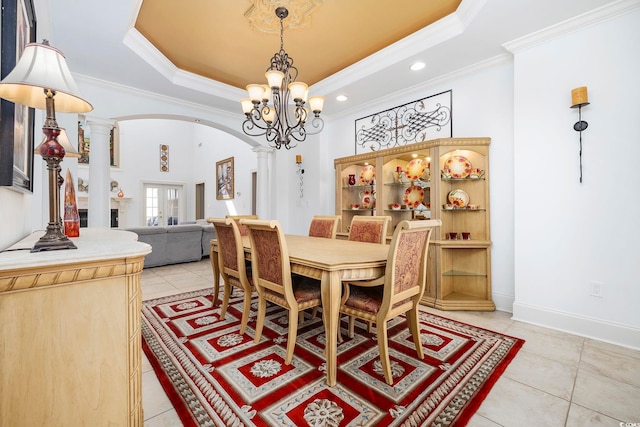 tiled dining space featuring ornamental molding, a raised ceiling, a chandelier, and ornate columns