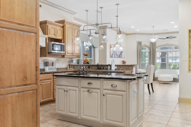 kitchen with a center island with sink, pendant lighting, dark stone counters, and a chandelier