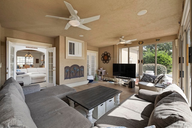 tiled living room with a textured ceiling, ceiling fan with notable chandelier, and french doors