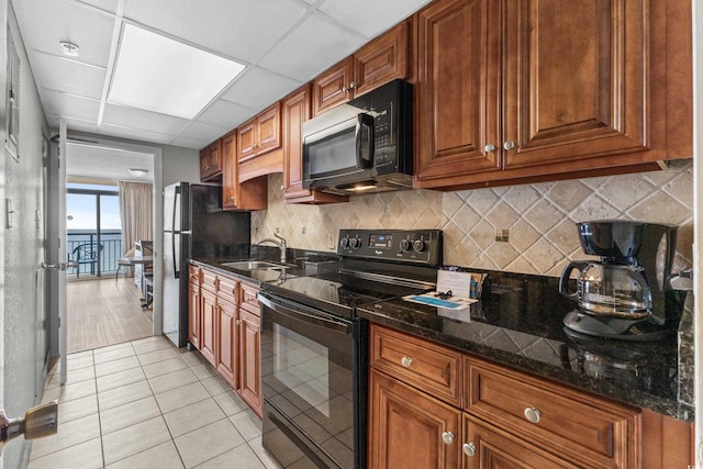 kitchen with a drop ceiling, sink, dark stone counters, light tile patterned floors, and black appliances