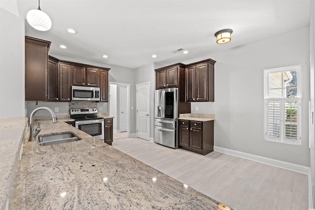 kitchen featuring light wood-style flooring, stainless steel appliances, a sink, dark brown cabinets, and light stone countertops