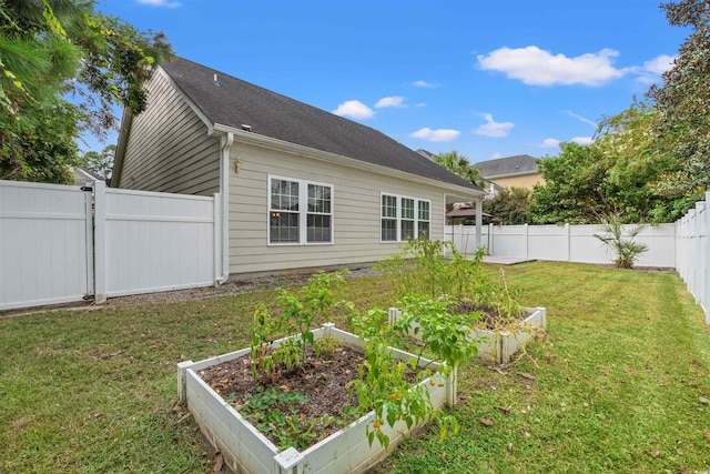 rear view of house featuring a vegetable garden, a fenced backyard, a yard, and roof with shingles