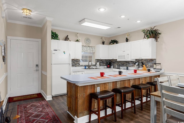 kitchen with white appliances, a kitchen bar, dark wood-type flooring, kitchen peninsula, and decorative backsplash